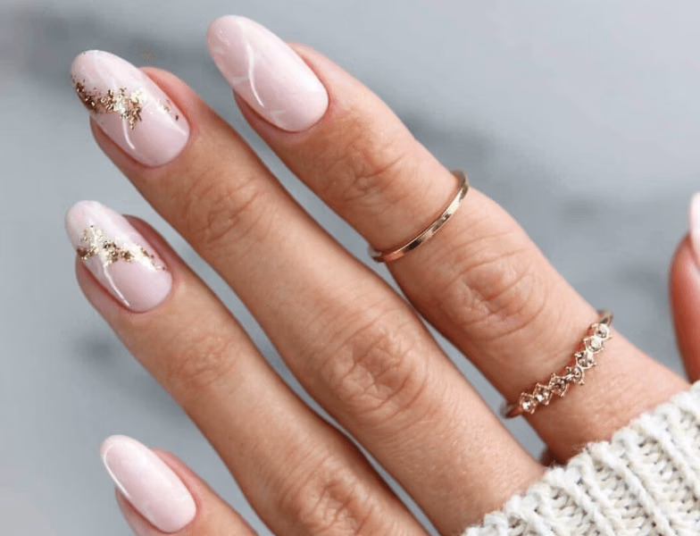 Close-up of elegant acrylic nails with soft pink base and gold foil nail art, showcasing custom nail extensions and shapes in Dubai salon