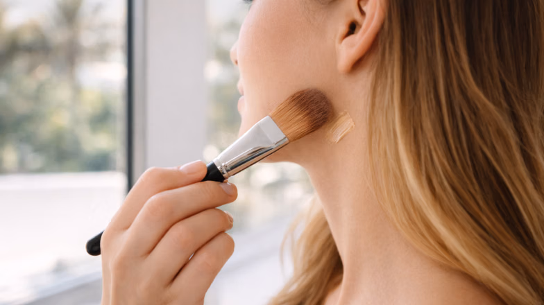 Woman applying foundation with a makeup brush along the jawline for even base coverage