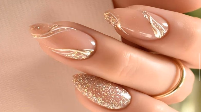Nude nails with gold abstract nail art and glitter accent design