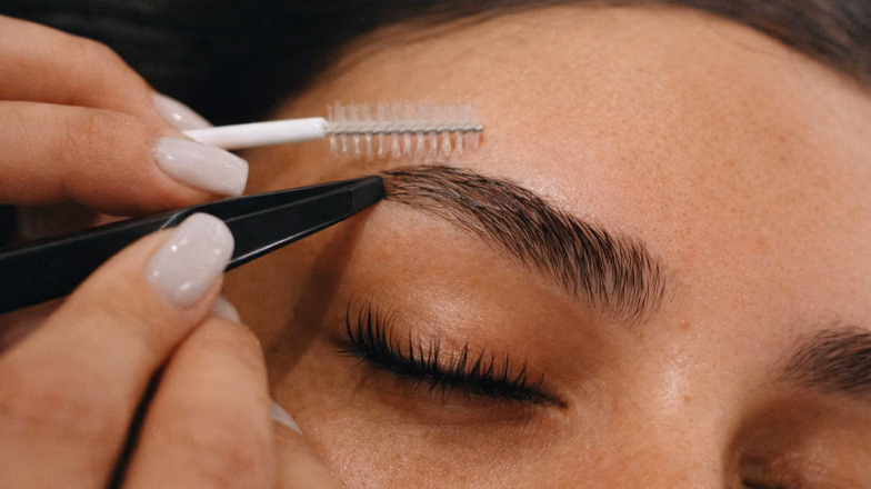 Eyebrow shaping procedure using tweezers during a professional brow mapping appointment