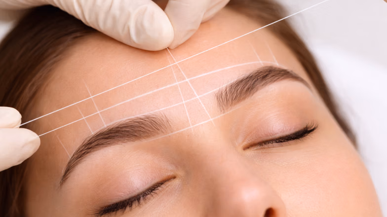 Brow mapping process with white thread marking eyebrow shape for precise symmetry and proportions