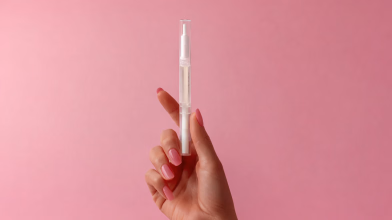 Hand holding a cuticle care tool against a soft pink background, illustrating gentle nail care routine