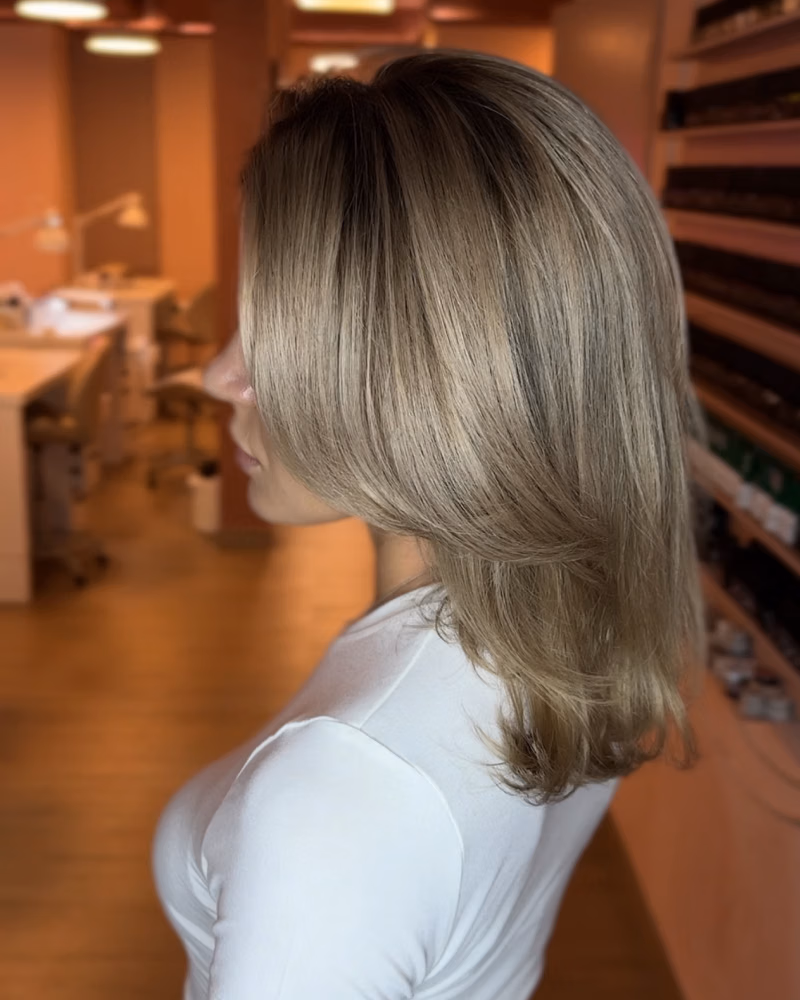 Woman with shoulder-length ash blonde layered hair after a smoothing and colour hair treatment, photographed from the side in a salon