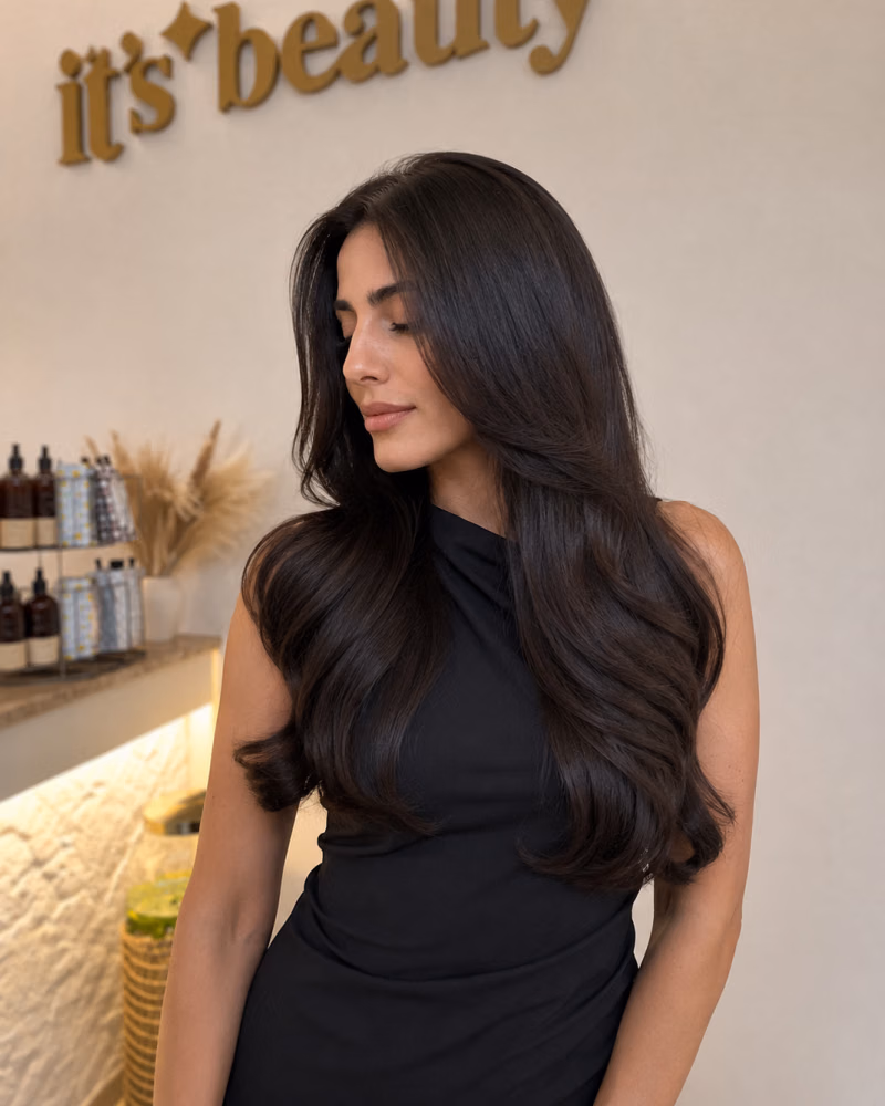 Woman with long, glossy brunette hair showcasing smooth texture and healthy shine after intensive hair care treatment