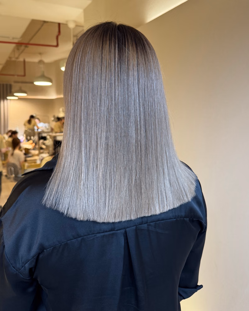 Back view of straight, shoulder-length icy ash blonde hair with a blunt cut, showing a fresh cool-toned hair color in a salon setting