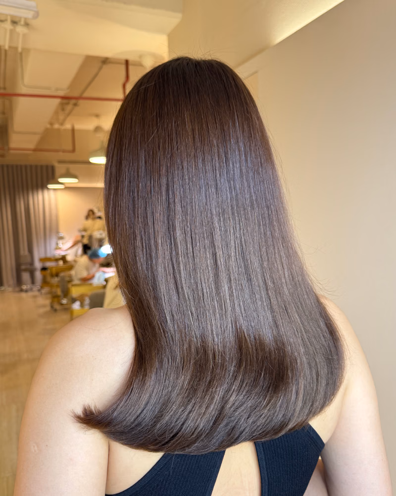 Back view of a woman with smooth, shoulder-length brunette hair after a hair loss treatment, showing healthy shine and fuller-looking hair in a salon setting