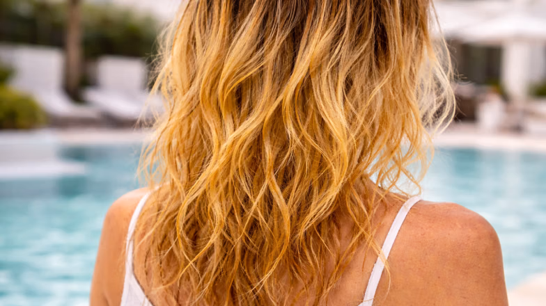 Sunlit wavy blonde hair near a pool, illustrating how heat and sun exposure affect hair pigment in hot climates