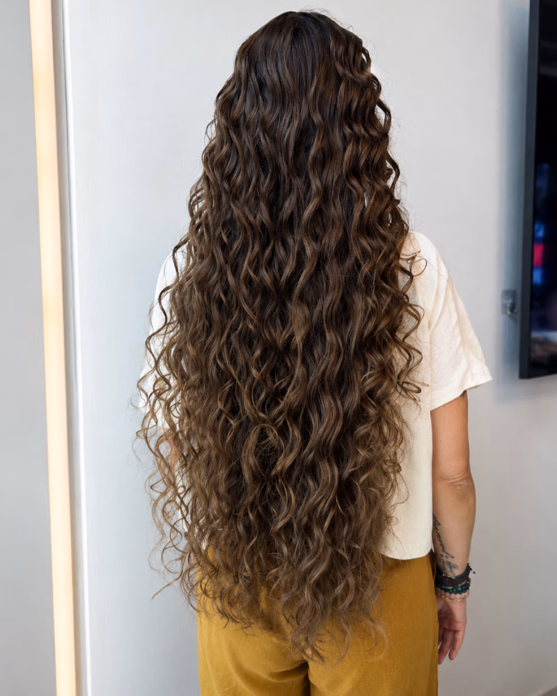 Back view of long, voluminous curly hair styled with loose waves and textured length