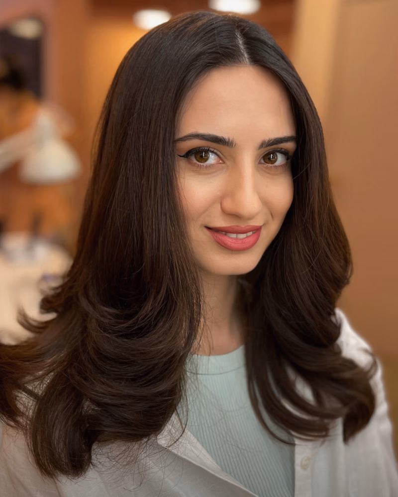 Woman with a smooth layered haircut and blow-dry, featuring soft face-framing layers and curled ends, in a salon