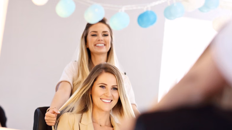 Hair stylist creating highlights for a smiling client in a beauty salon with soft lighting