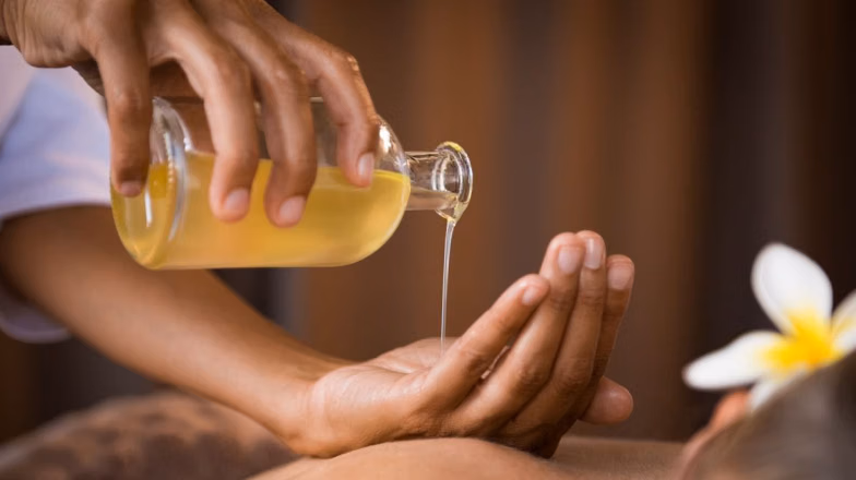 Massage therapist pouring oil onto hands before starting a relaxing massage treatment
