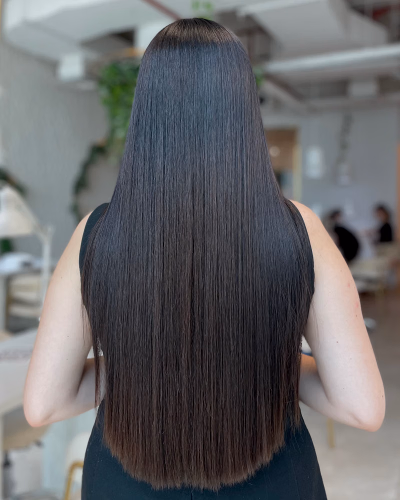 Back view of long, straight, glossy dark hair after a keratin treatment in a salon