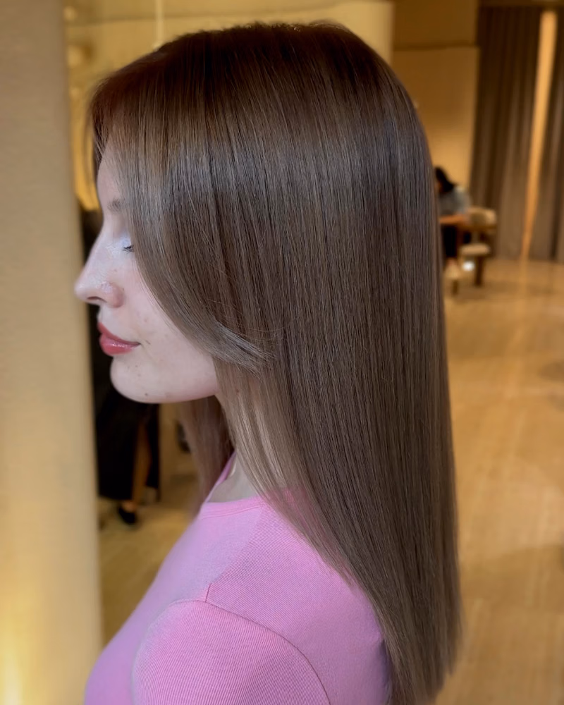 Side profile of a woman with smooth, straight, glossy light brown hair after a keratin treatment in a salon