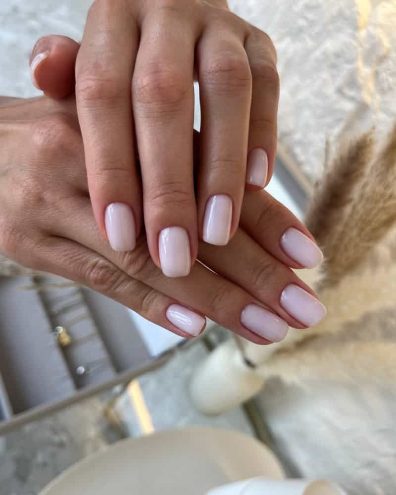 a close-up of hands with glossy baby pink gel nails in a soft square shape
