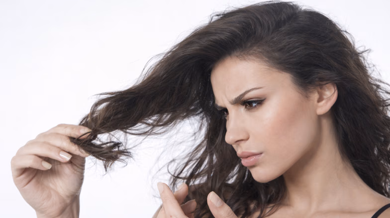 Woman inspecting her dry, tangled hair, showing signs of moisture deficiency