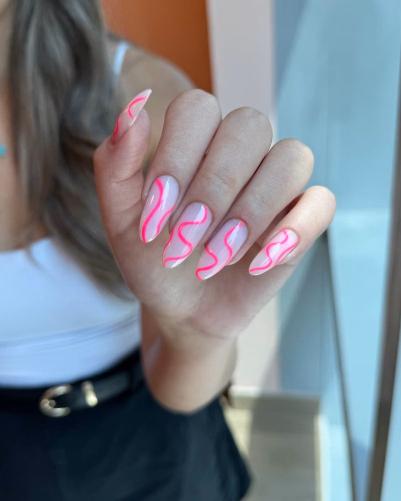 Long almond-shaped nails with a soft pink base and glossy neon pink swirl nail art design