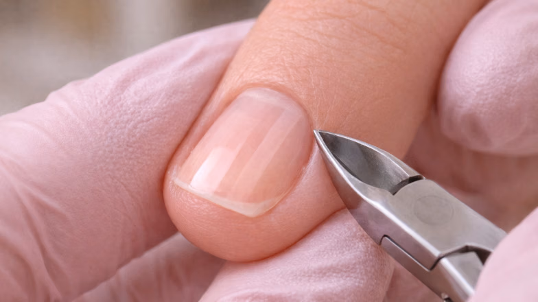 Nail technician removing cuticle during manicure to improve coating adhesion