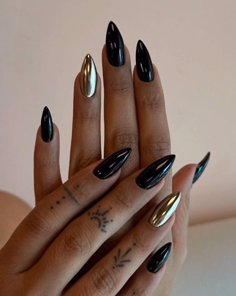 hands with long almond-shaped nail extensions, featuring glossy black polish and gold chrome accent nails
