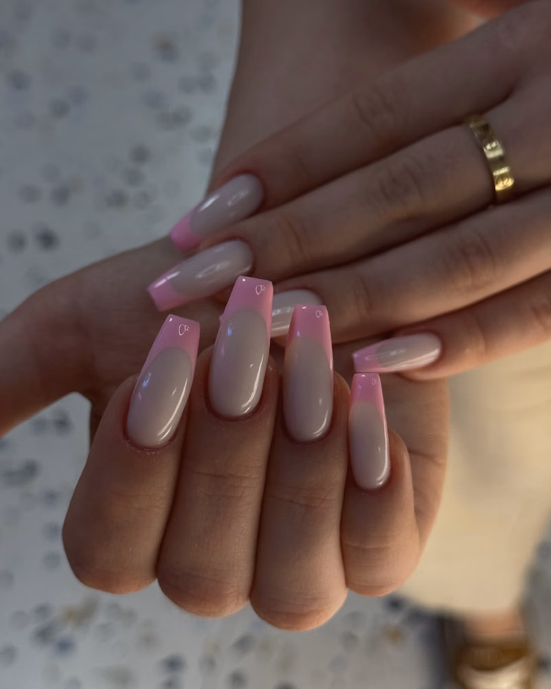 hands with glossy nude pink gel nails and soft pink french tips in a square shape, photographed in warm indoor light