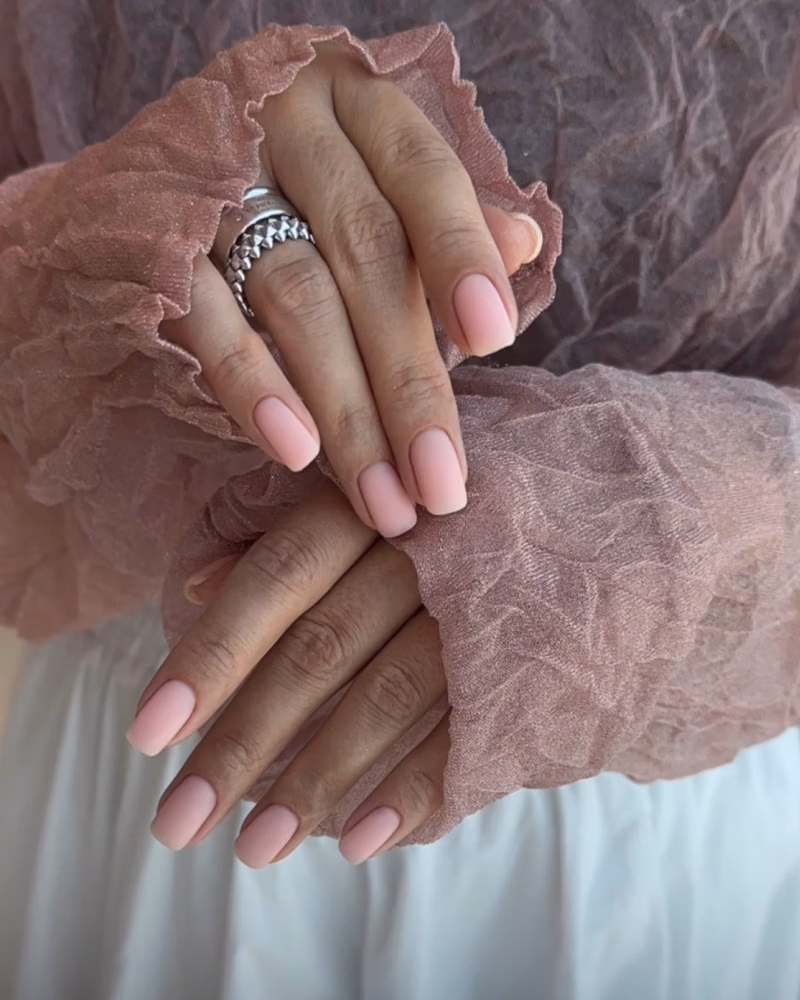 hands with a soft pale pink manicure and squared nails, framed by sheer dusty rose ruffled sleeves and silver rings