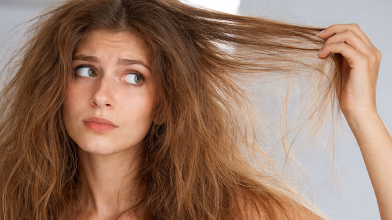 Woman examining her dry, frizzy hair and pulling a strand to show damage and stiffness from protein overload