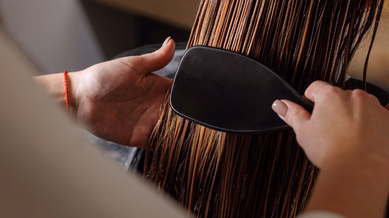 Hair stylist brushing long hair during hair botox treatment process in a salon