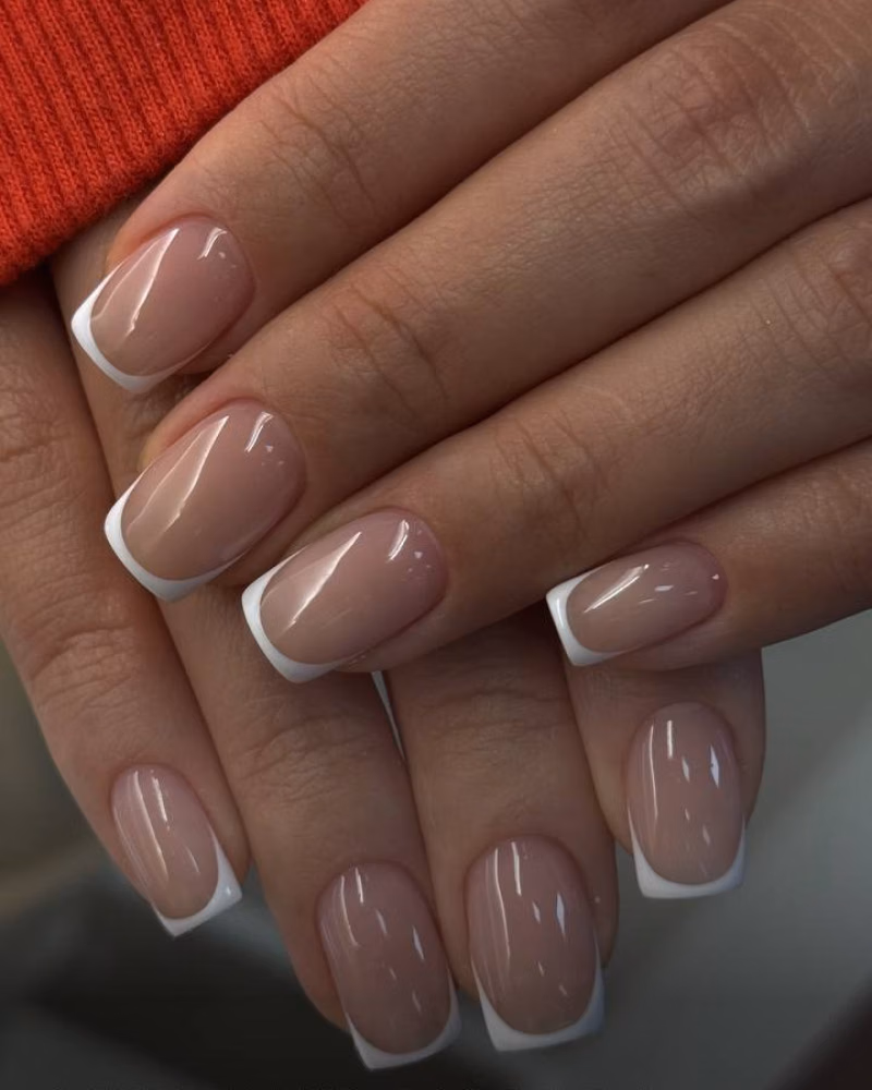glossy nude-and-white French tips on square nails, showing a clean Russian manicure finish against a red sleeve