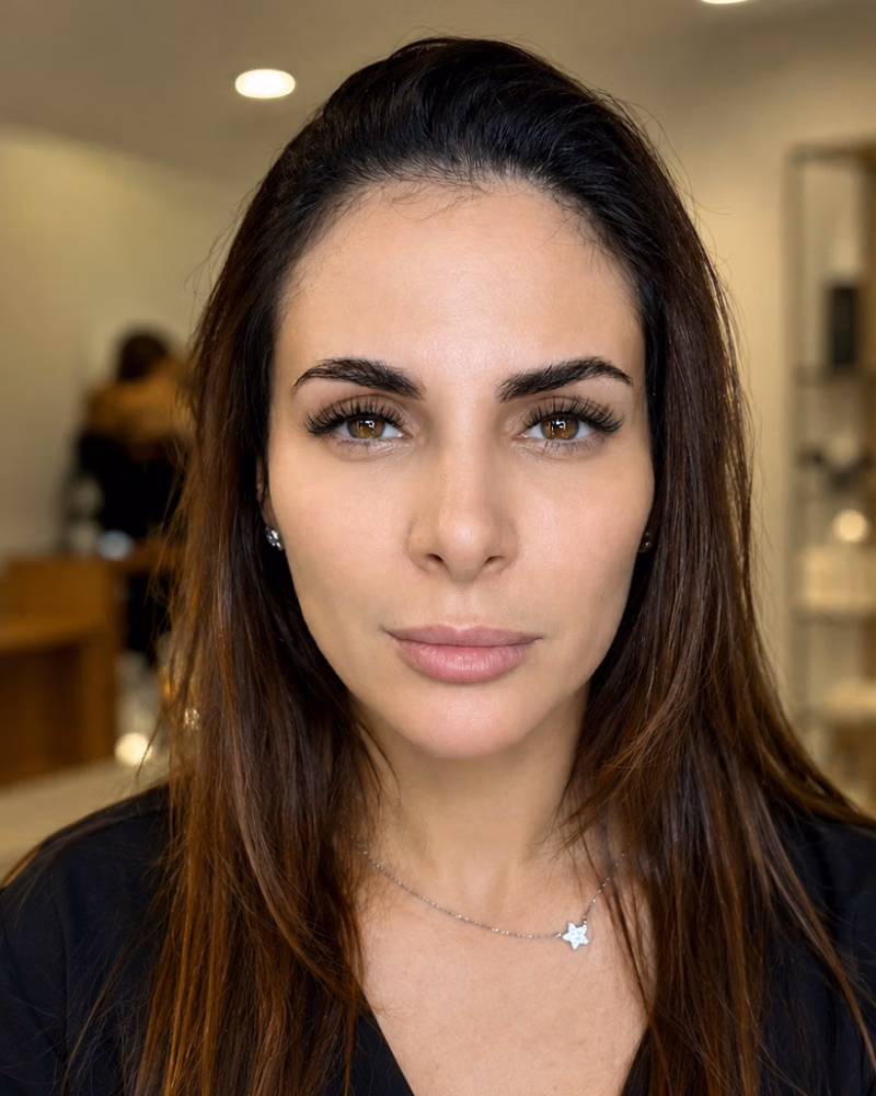 woman with softly lifted Russian volume lashes, natural brows, and glossy lips, wearing a black top and delicate necklace in bright indoor lighting