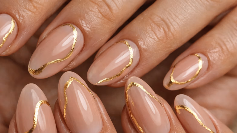 Minimalist nail art with gold foil accents on nude almond-shaped nails