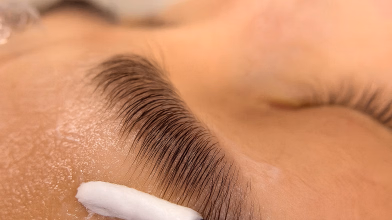 Applying solution to eyebrows during brow lamination procedure in salon