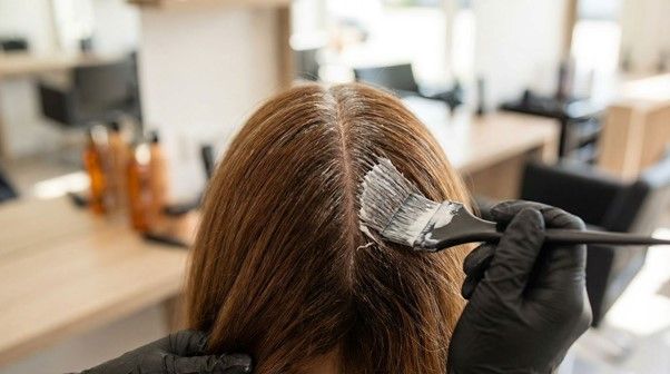 Hair stylist applying color to roots during regrowth touch-up in a salon